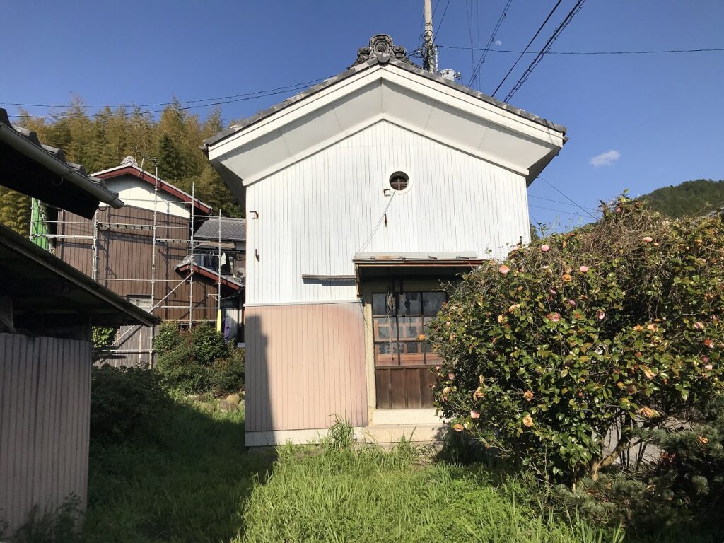滋賀県犬上郡の空き家「円城寺邸」に付属する蔵の外観。切妻屋根と白い外壁、正面に丸窓と木製引き戸がある建物