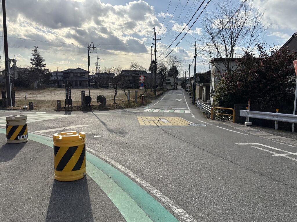 黄色と黒のバリケードが設置された交差点。株式会社丸由へ向かう際は、ここを道なりに右へ進みます。