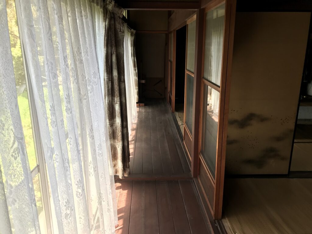 滋賀県犬上郡の空き家「円城寺邸」の南側廊下。障子とガラス戸、レースカーテン越しに庭が見える木造の縁側