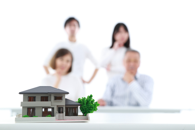空き家や不動産の管理について悩む家族のイメージ写真。家の模型を前に考え込む姿。